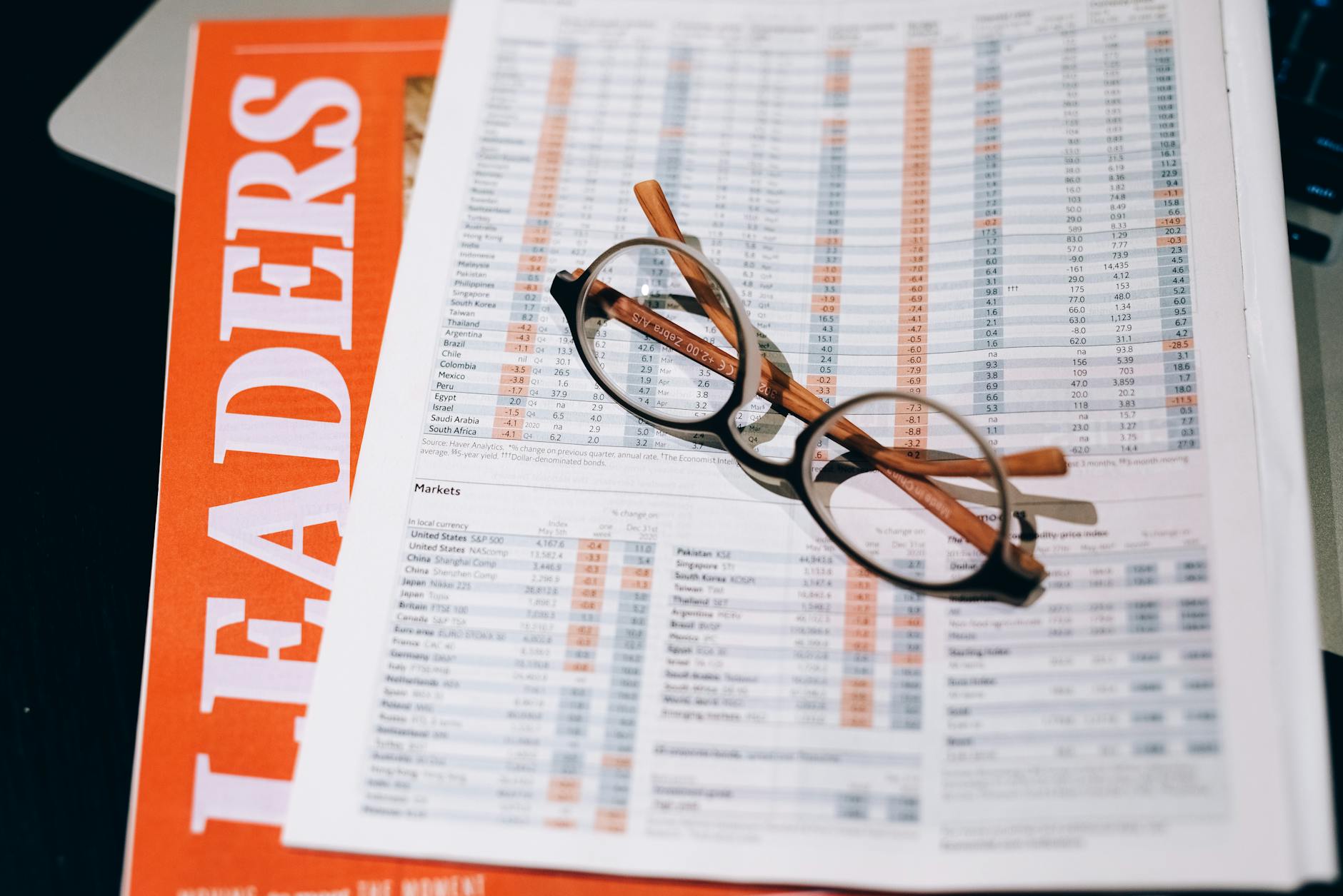 Ilustrasi: A pair of eyeglasses resting on a financial document and magazine with bold headline "LEADERS" in focus.
