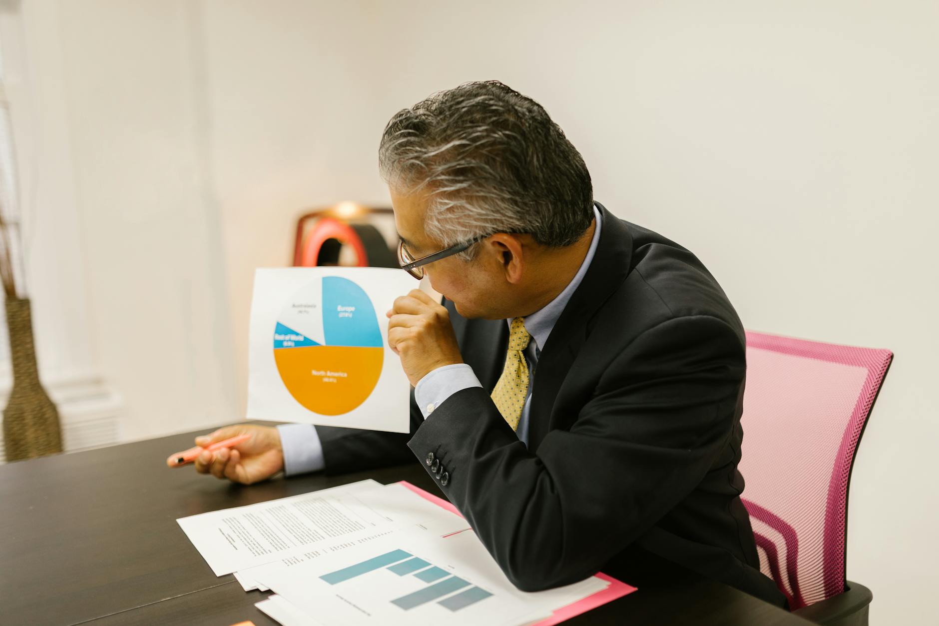 Ilustrasi: A businessman in a suit reviews pie chart documents at his office desk.