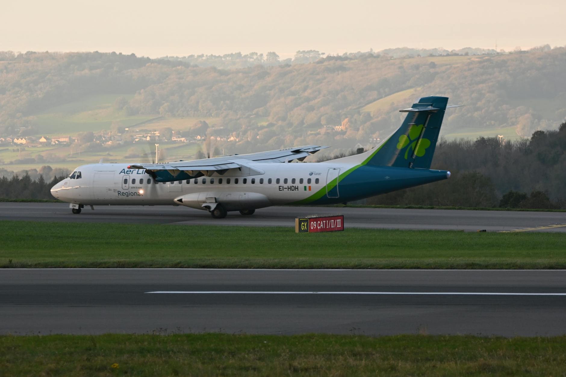 Ilustrasi: Aer Lingus ATR aircraft taxiing on the runway during sunset with a scenic landscape in the background.