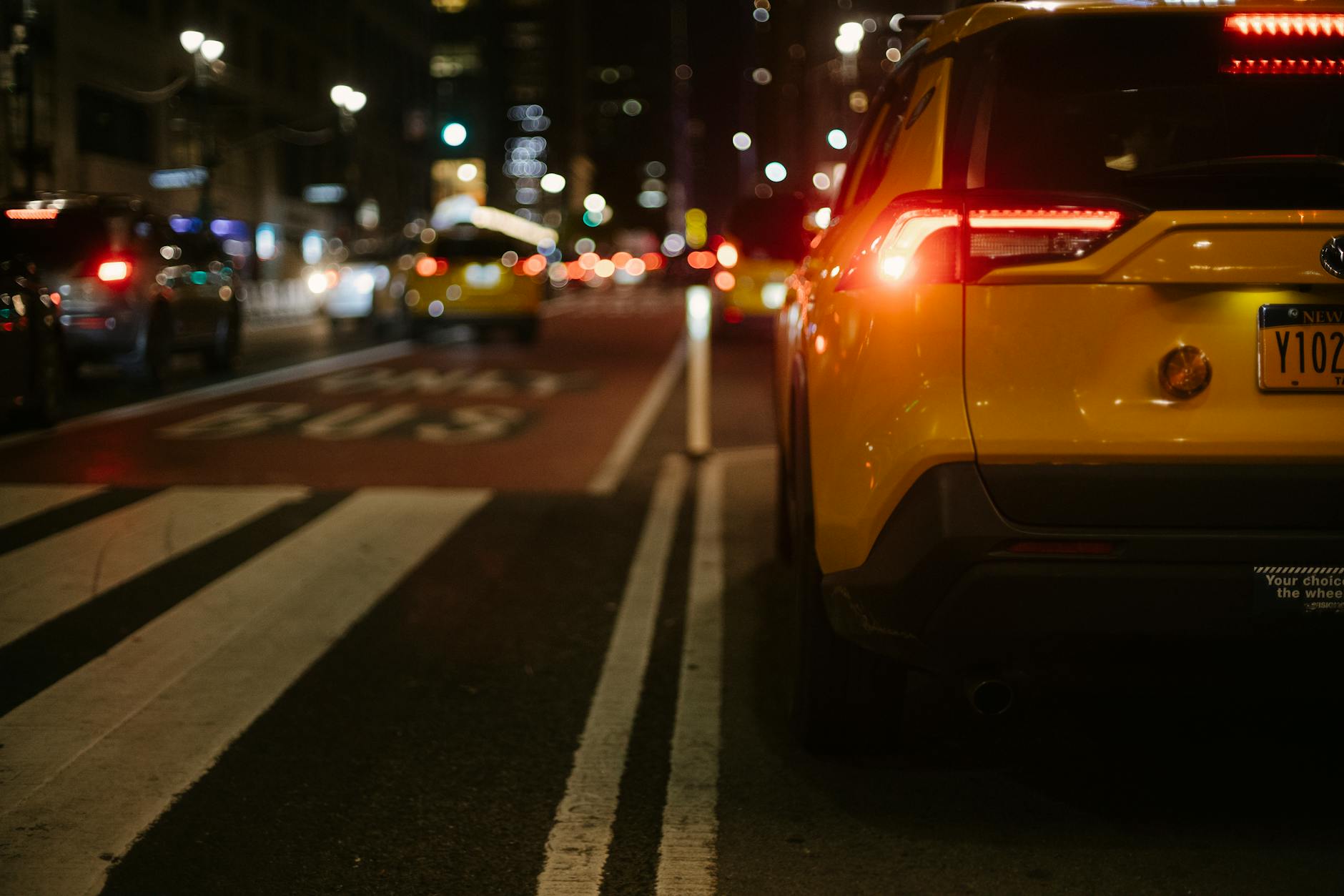 Ilustrasi: Shiny yellow crossover taxi car driving on marked asphalt road in modern illuminated city malam hari
