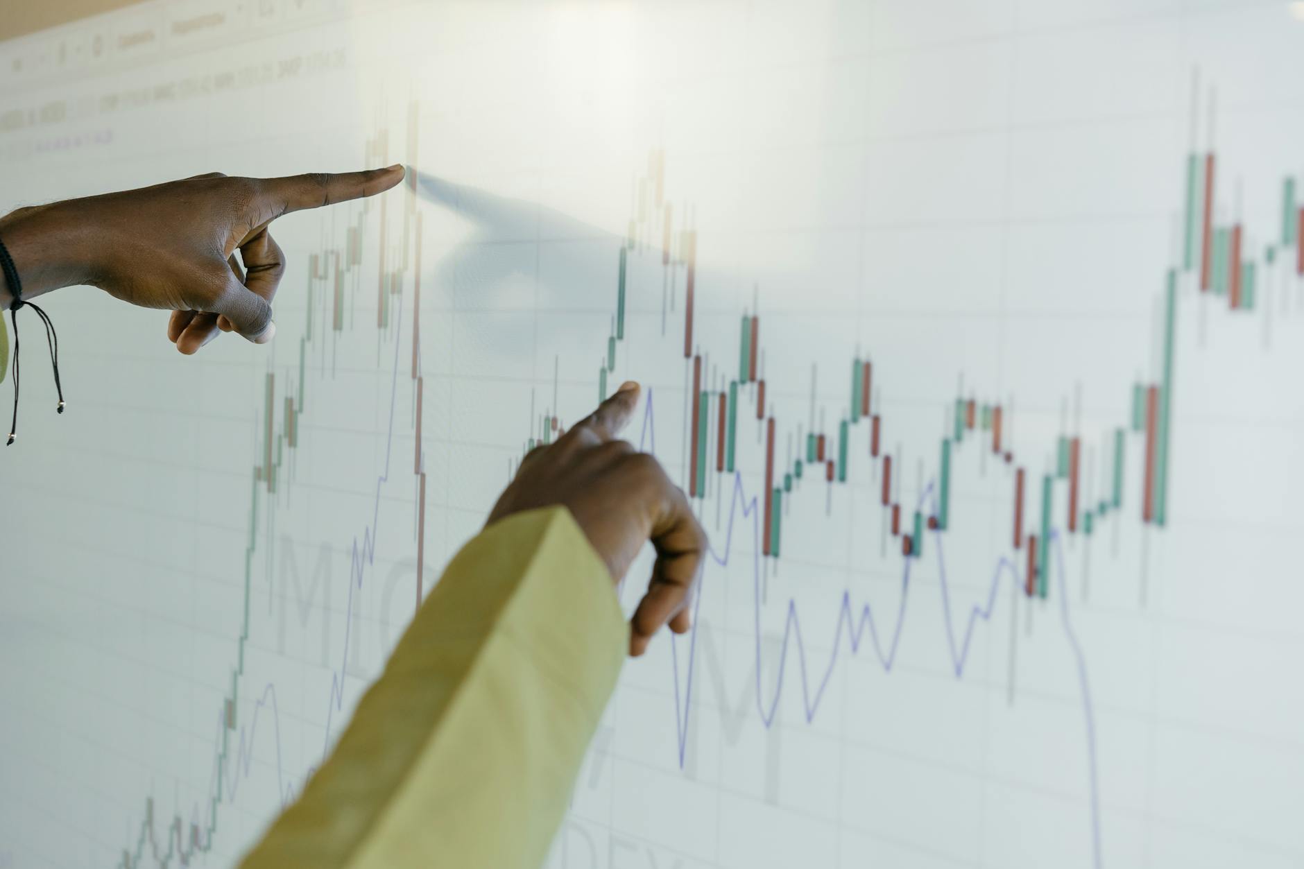Ilustrasi: Hands pointing at a financial stock chart on a digital screen, highlighting data analysis and trends.