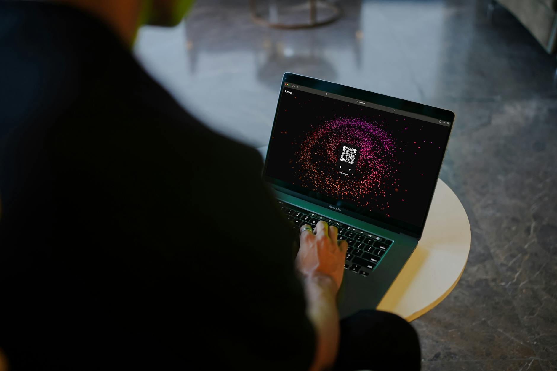Ilustrasi: A person interacts with a colorful QR code display on a laptop in a modern indoor setting.
