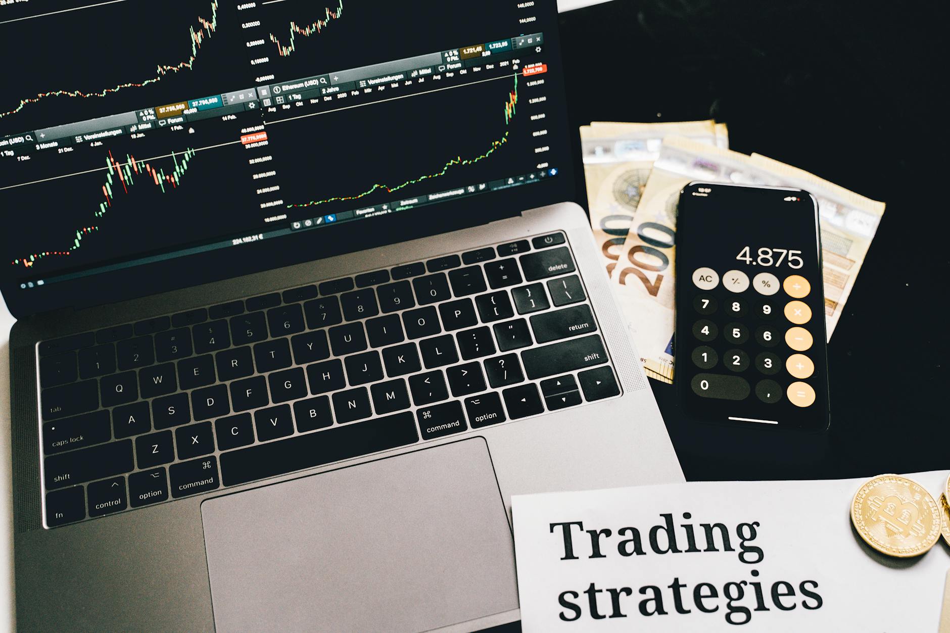 Ilustrasi: A laptop showing stock market graphs with a smartphone calculator, euro bills, coins, and trading strategies paper.