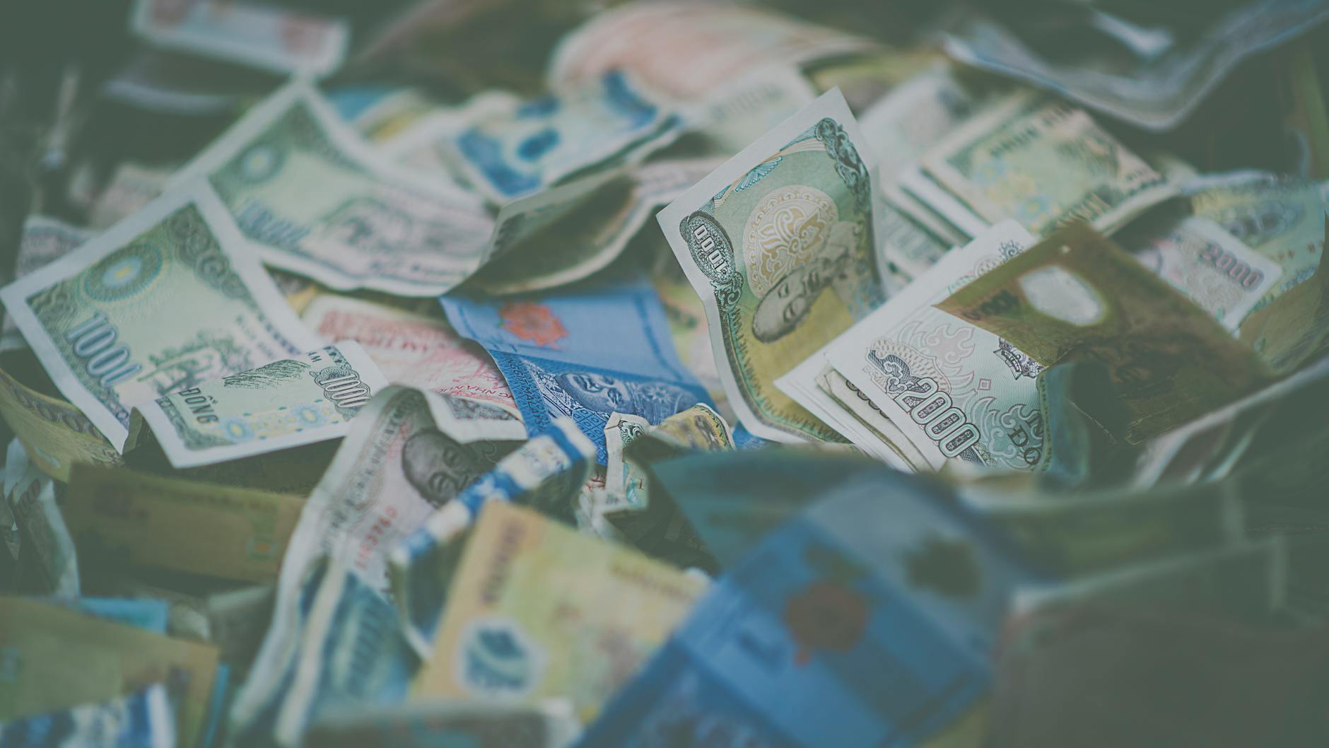 Ilustrasi: A close-up view of diverse international currency banknotes in soft focus, conveying wealth and finance themes.