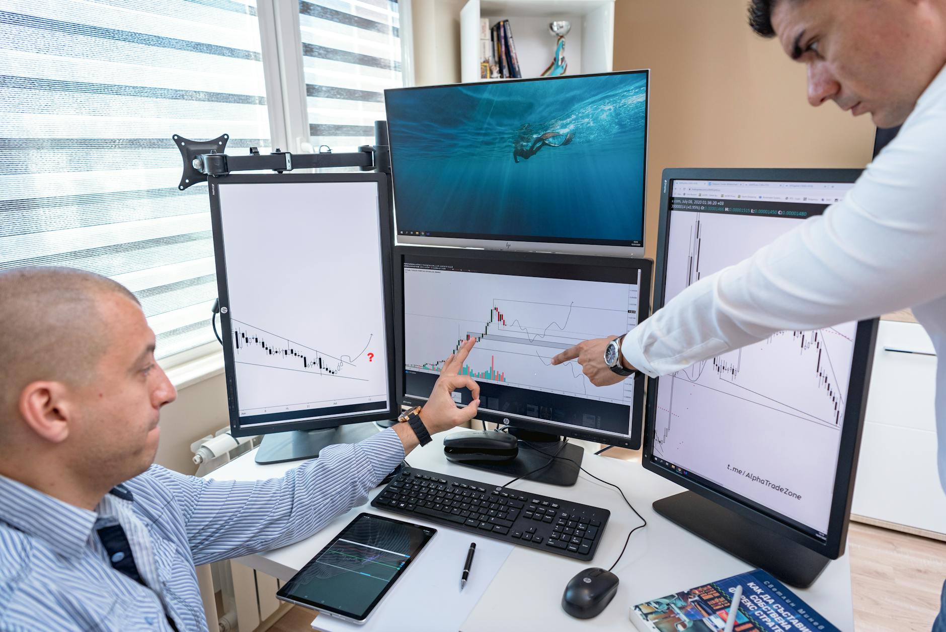 Ilustrasi: Two business professionals analyzing financial data on multiple computer screens in an office setting.